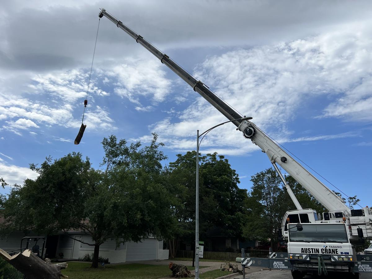 Crane lifting a large trunk section during a tree removal job in Austin